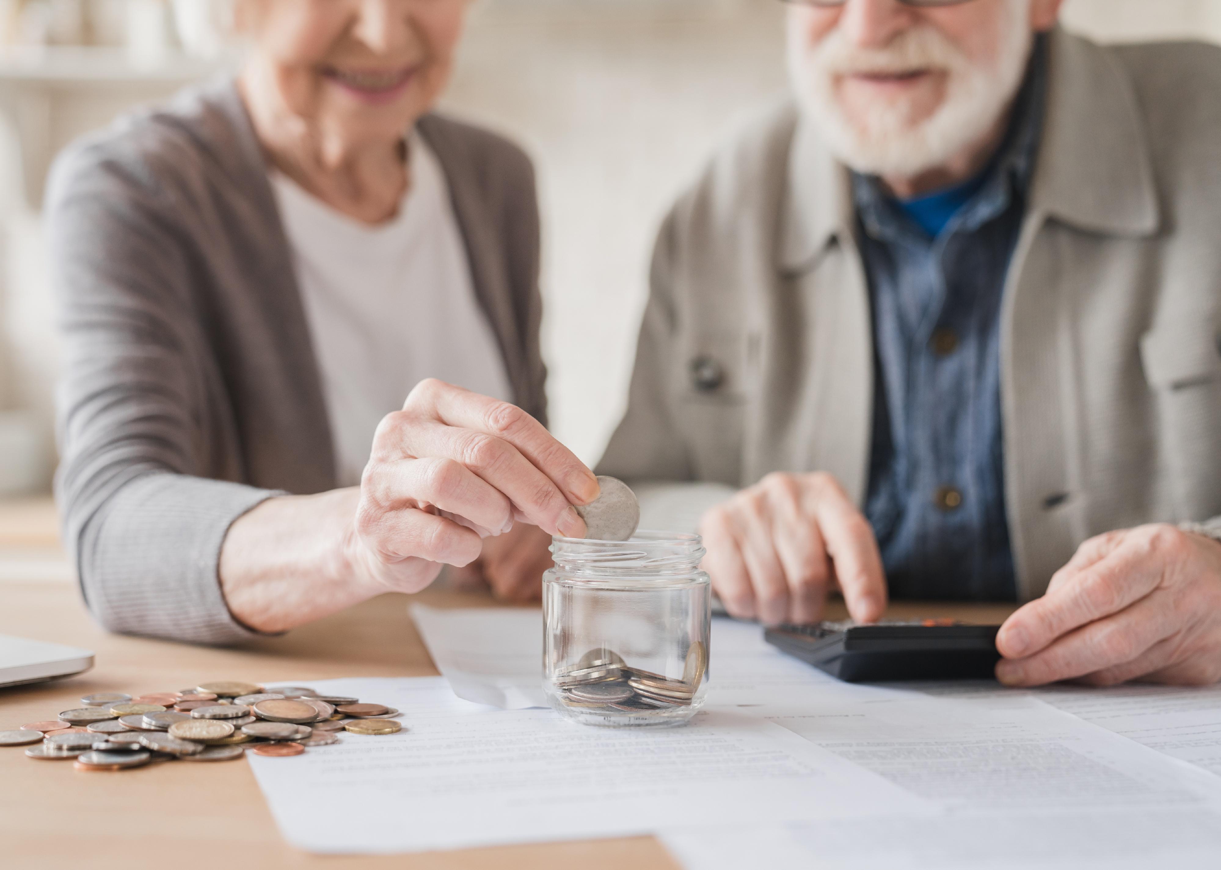 Elderly couple putting coin into money box.