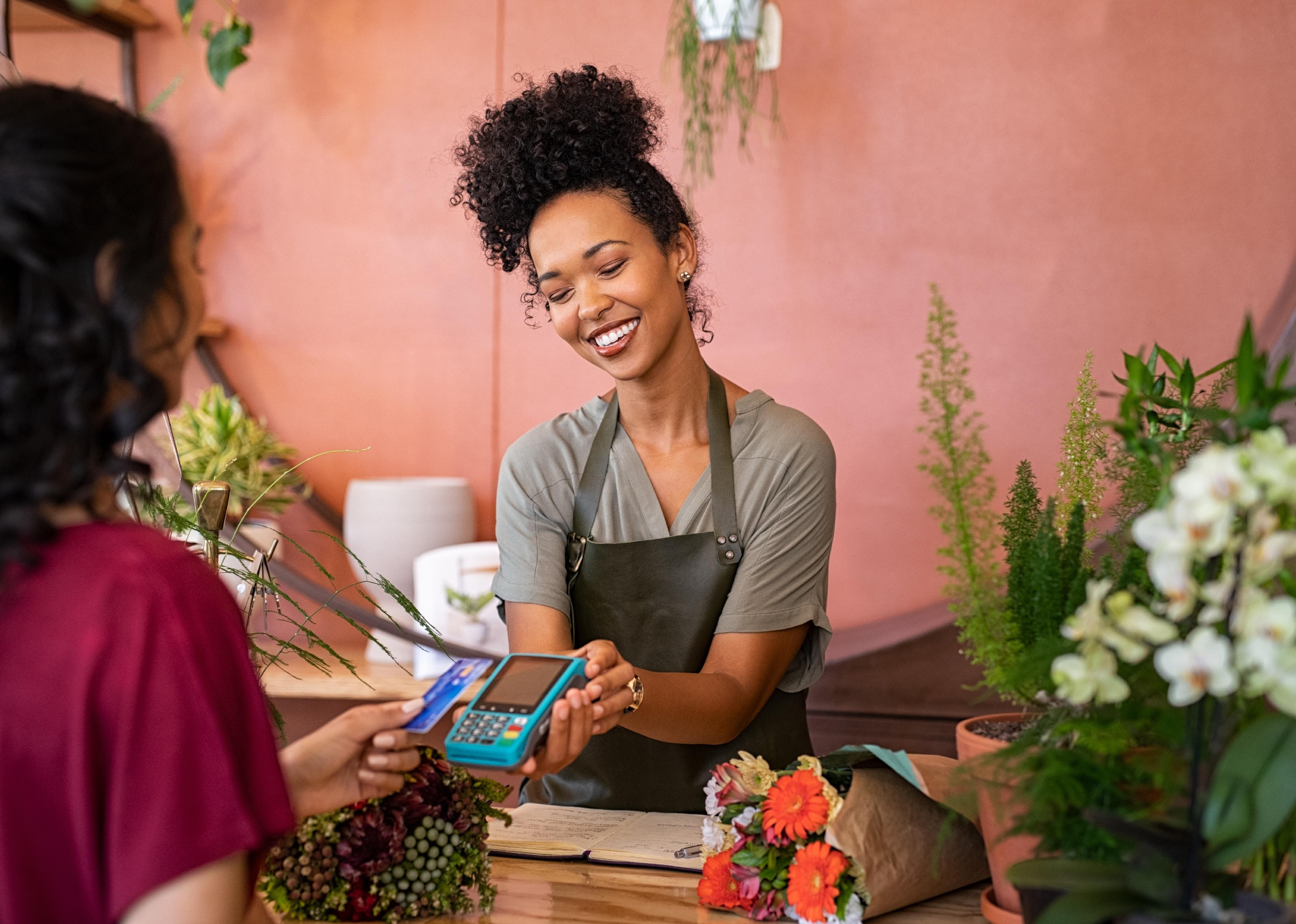 Smiling florist holding card reader machine with customer paying with credit card.