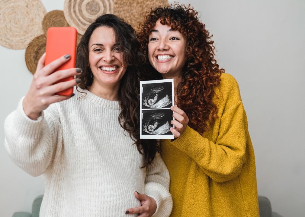 Two women holding ultrasound photo wile looking at phone