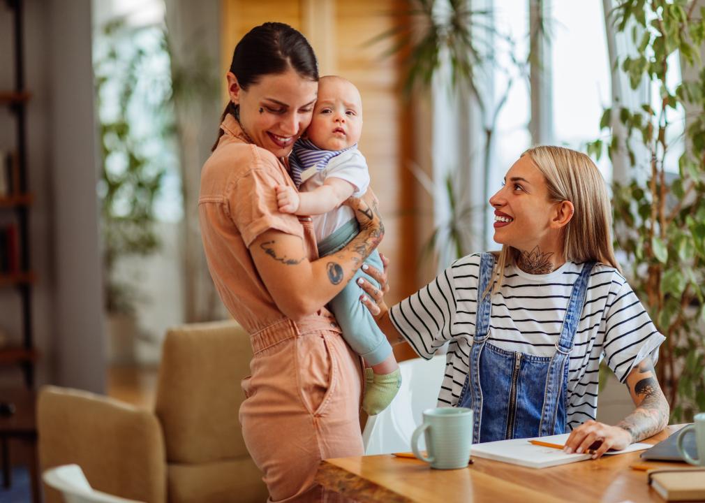 Woman holding baby, standing next to woman sitting at table