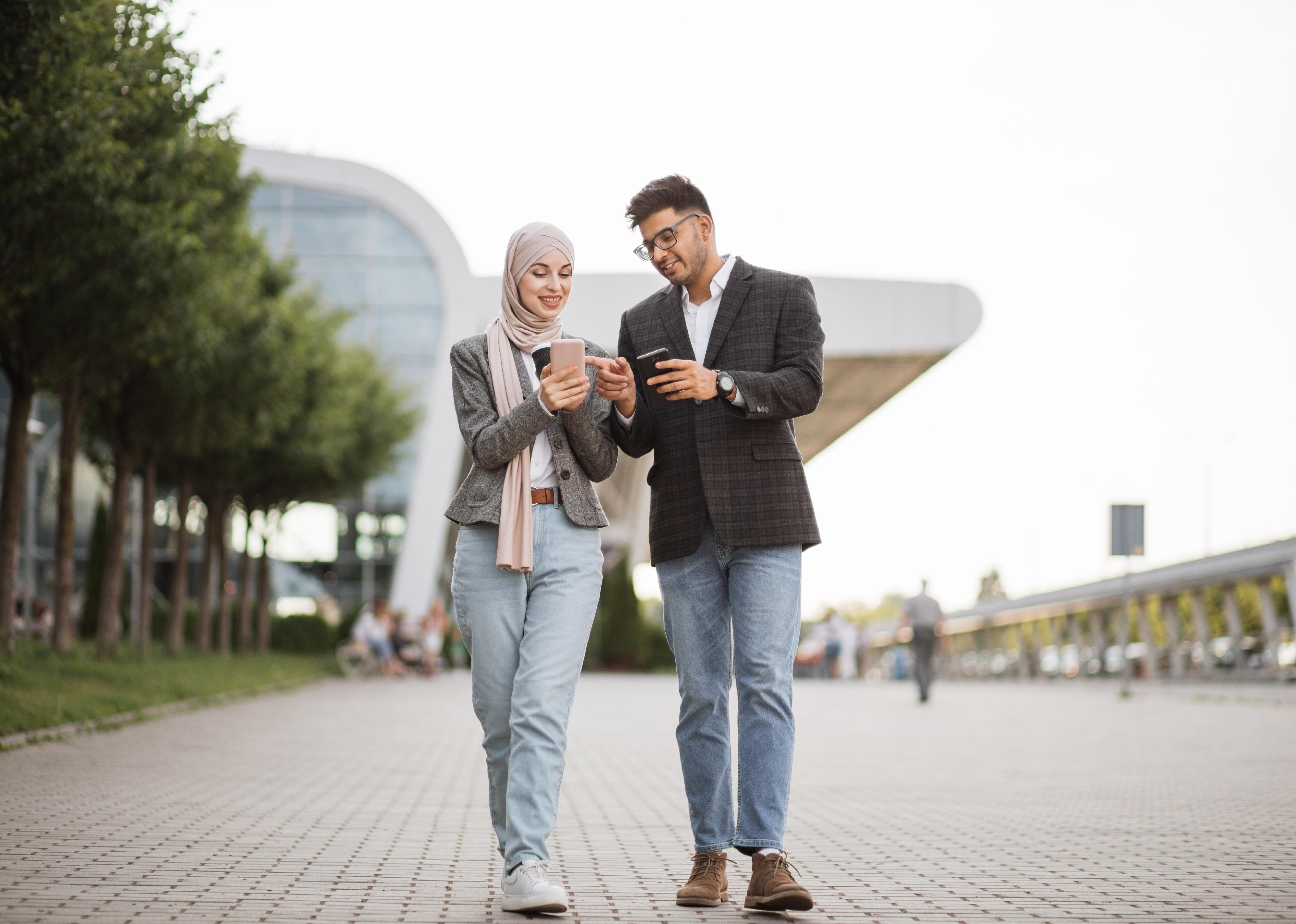 Front view of a man and woman walking on the street with smartphones.