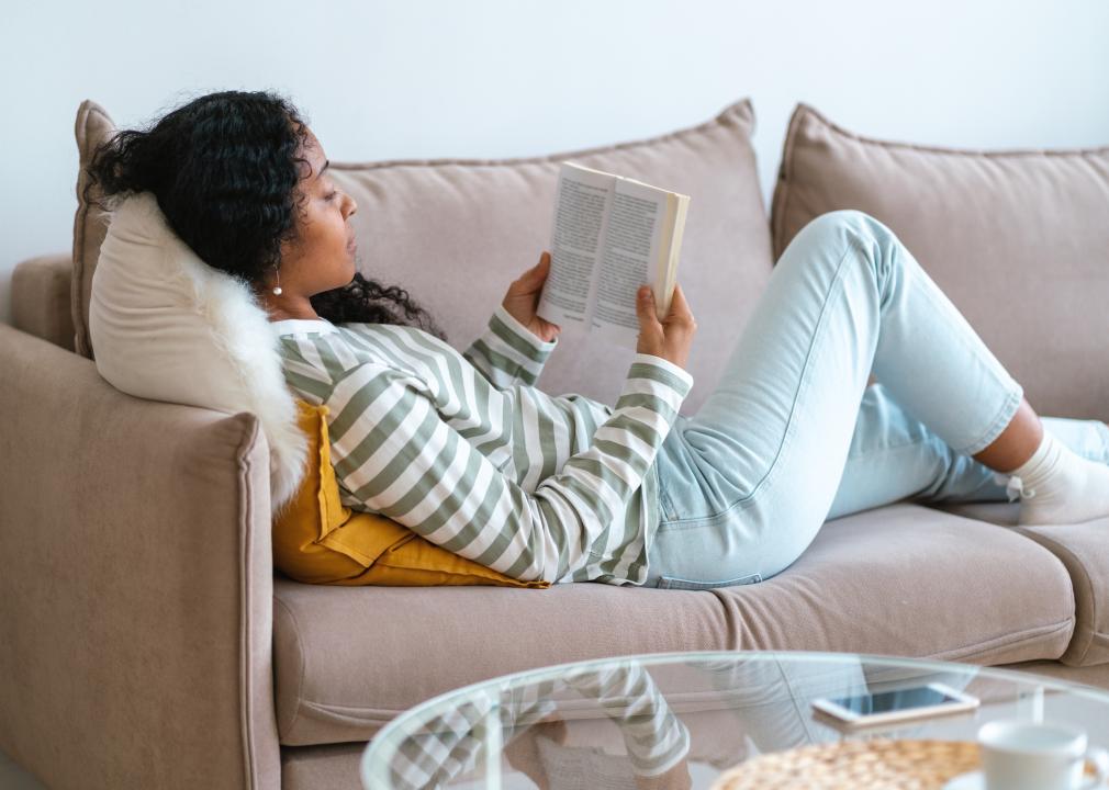 Woman laying on couch and reading a book.