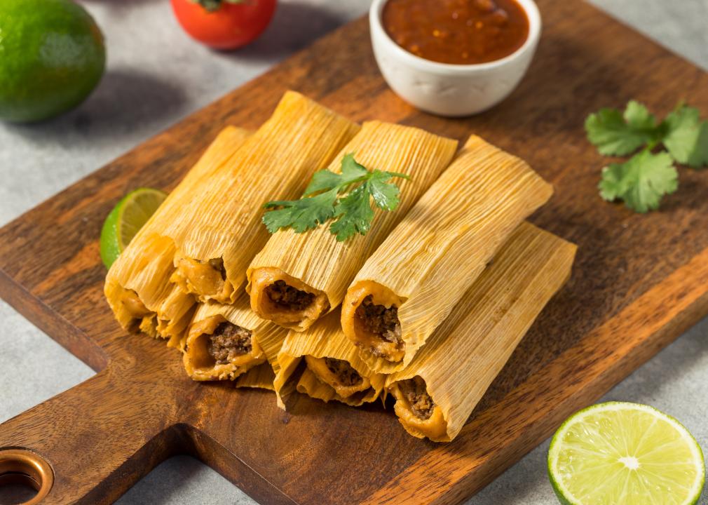 Homemade beef tamales with fresh cilantro sprinkled on top on a wooden serving board with a small bowl of salsa and a cut lime. 