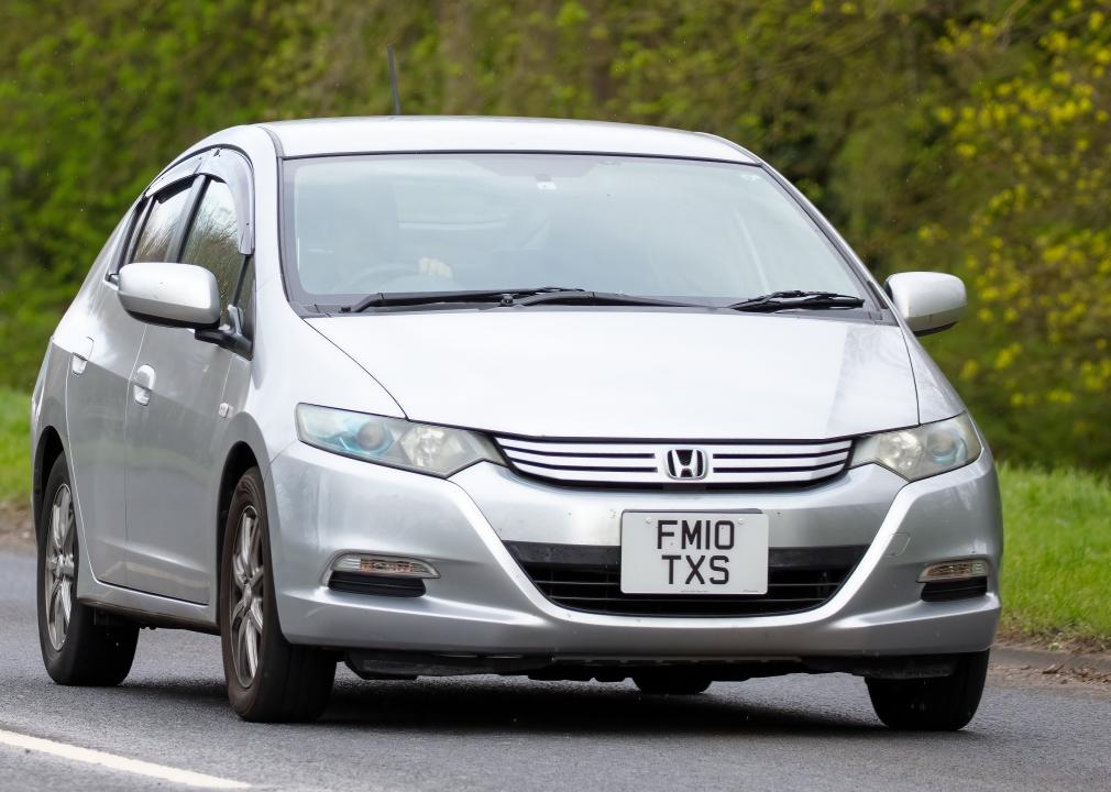 Honda Insight car with a U.K. license plate driving on an country road.