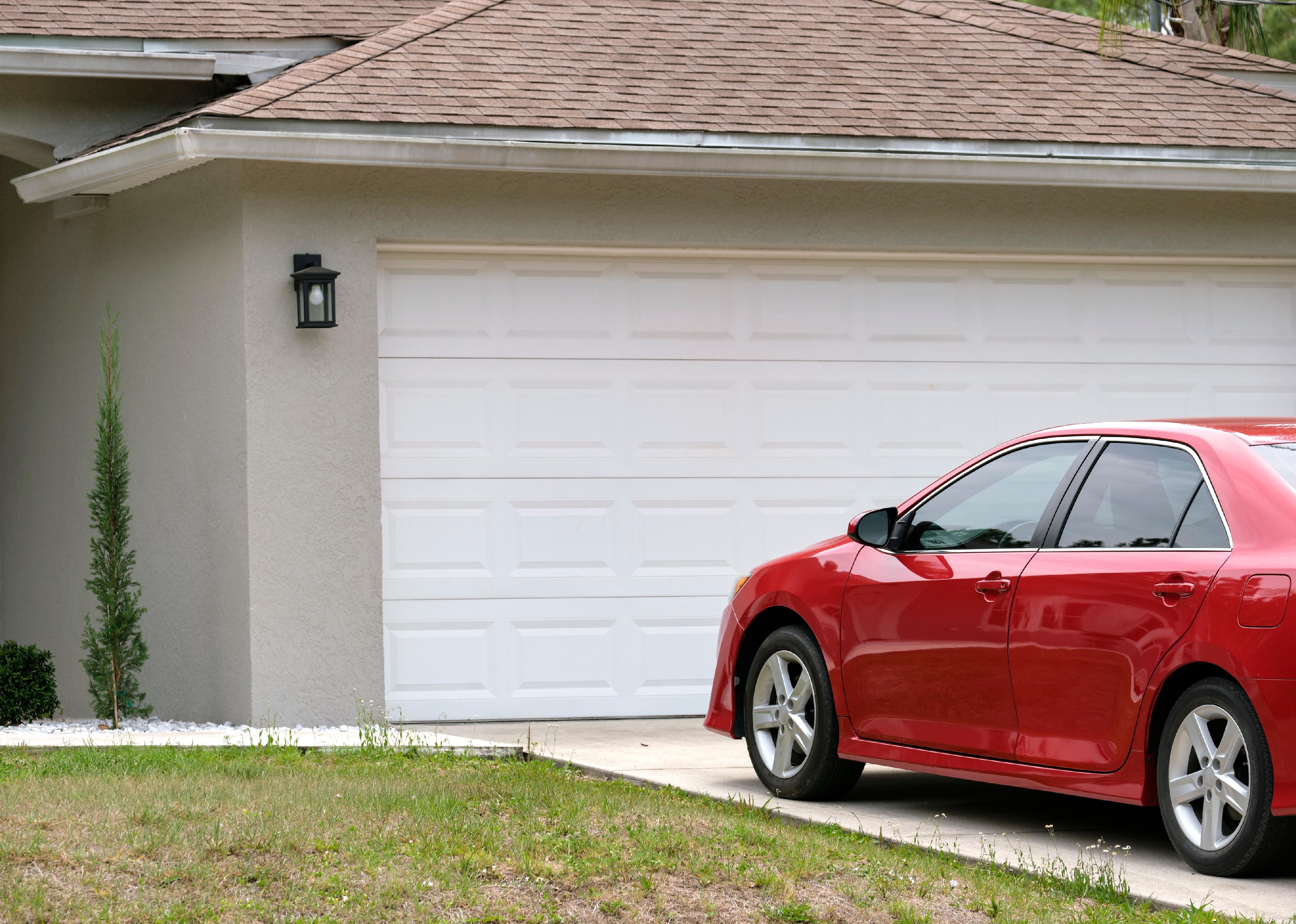 Car parked in front of wide garage double door on concrete driveway.