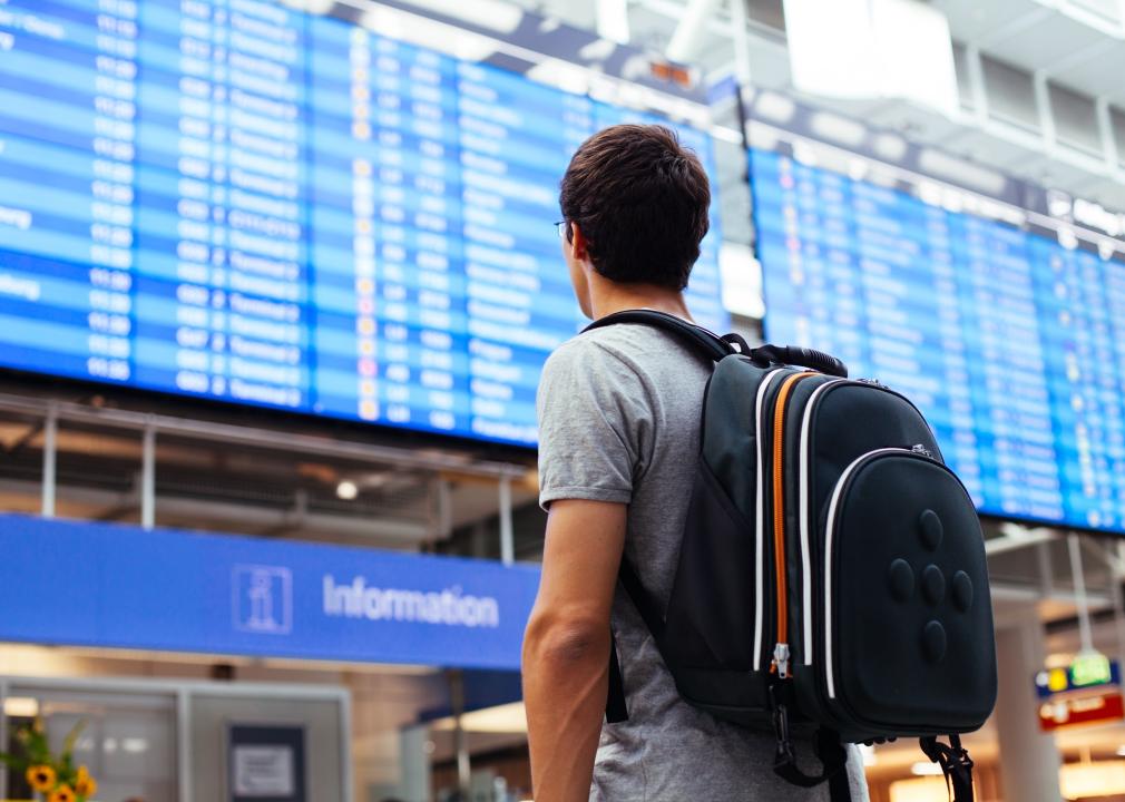 Young man with backpack in airport near flight status screen.