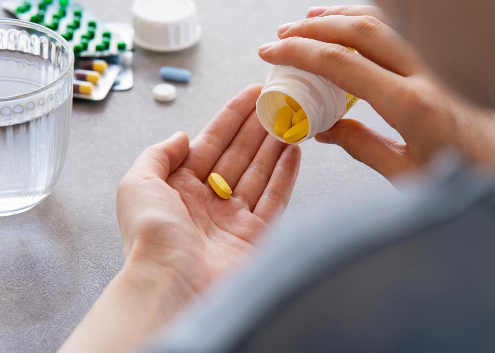 Close up person holding a pill in their hand with a glass of water on the table.