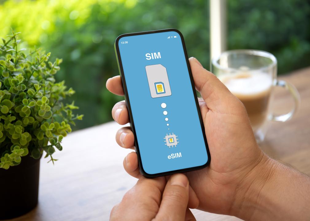 Hands holding a phone with the screen showing an image of a SIM card with five dots decreasing in size, leading to a smaller image of an eSIM.