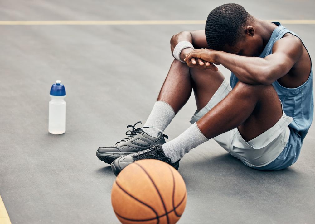 Young boy sitting on basketball court with head between hands.