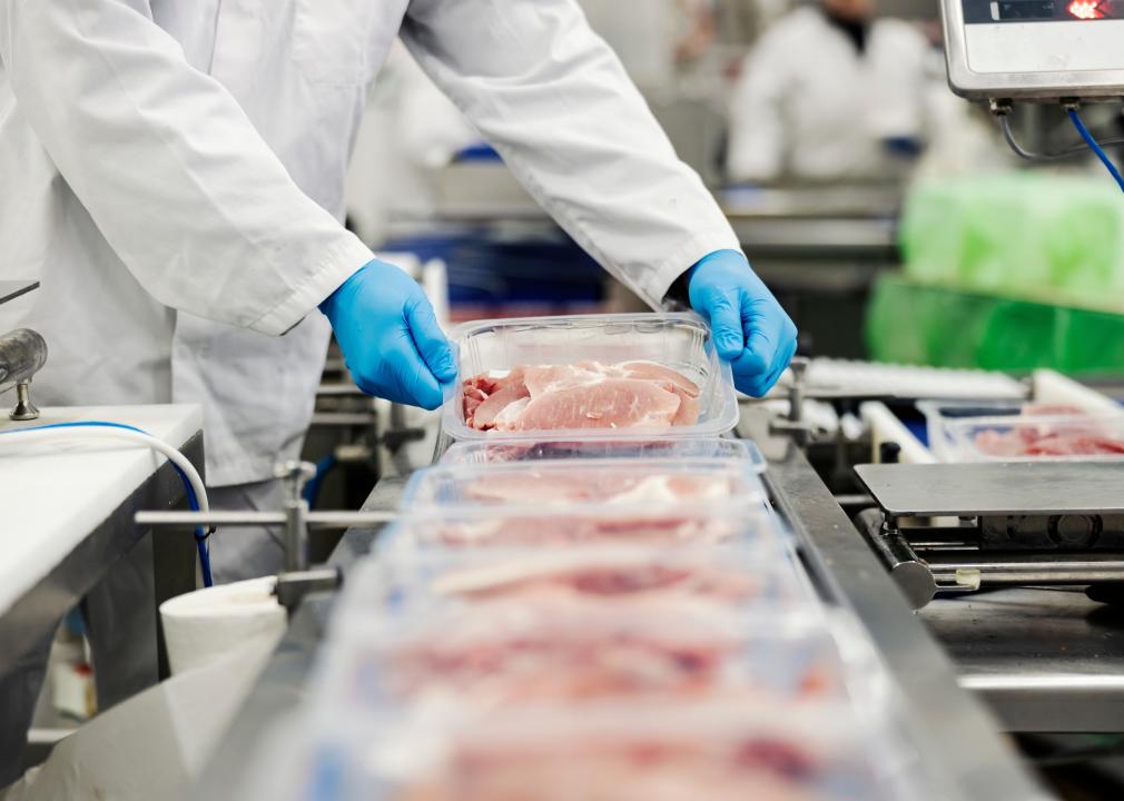 Worker gathering packed meat on a conveyor belt.