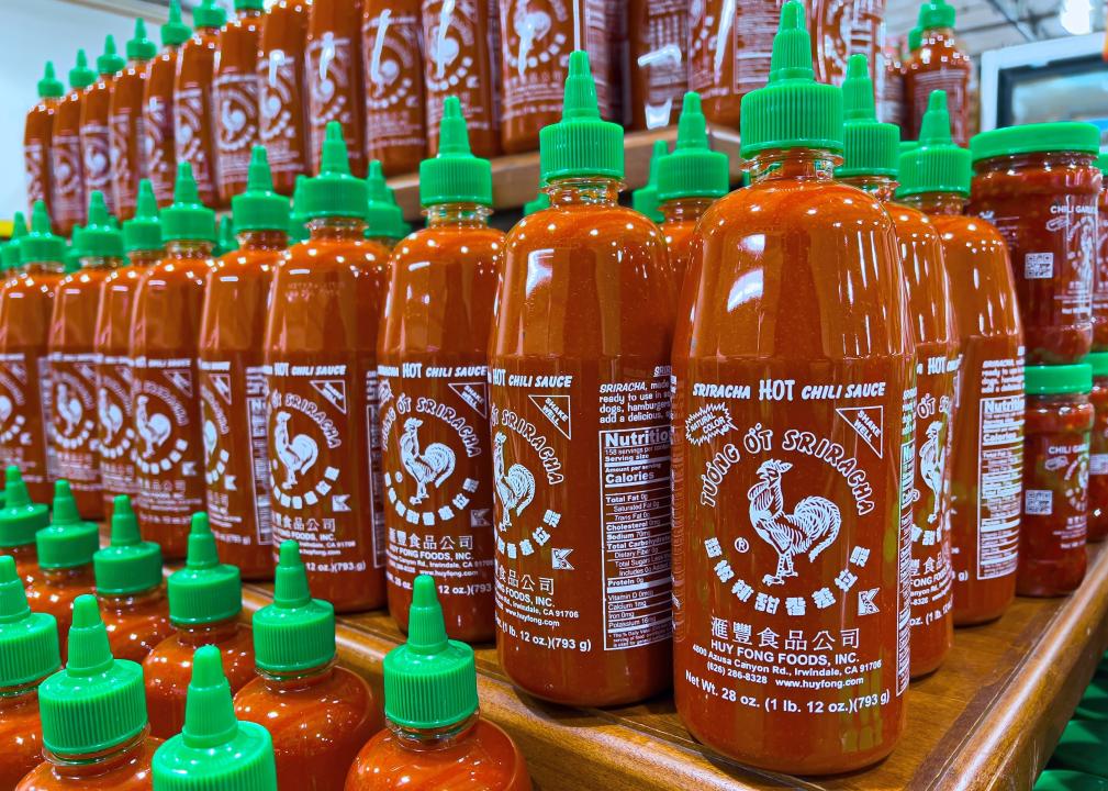 Plastic bottles of Huy Fong Food Sriracha sauce in a supermarket aisle.