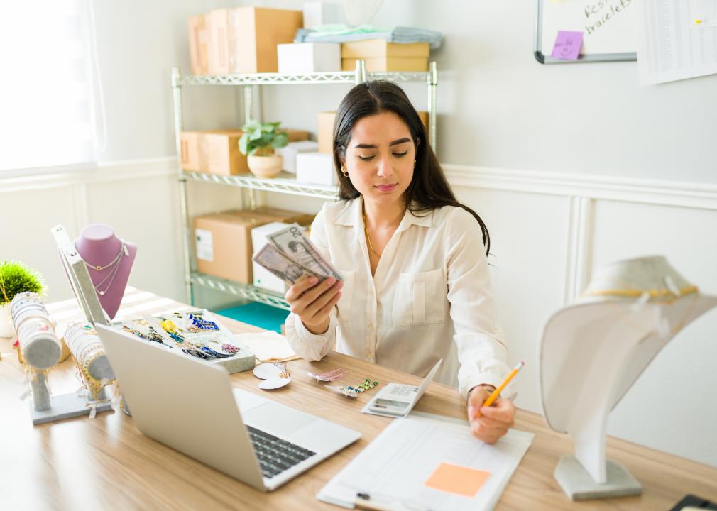 A woman counting money surrounded by jewelry inventory.