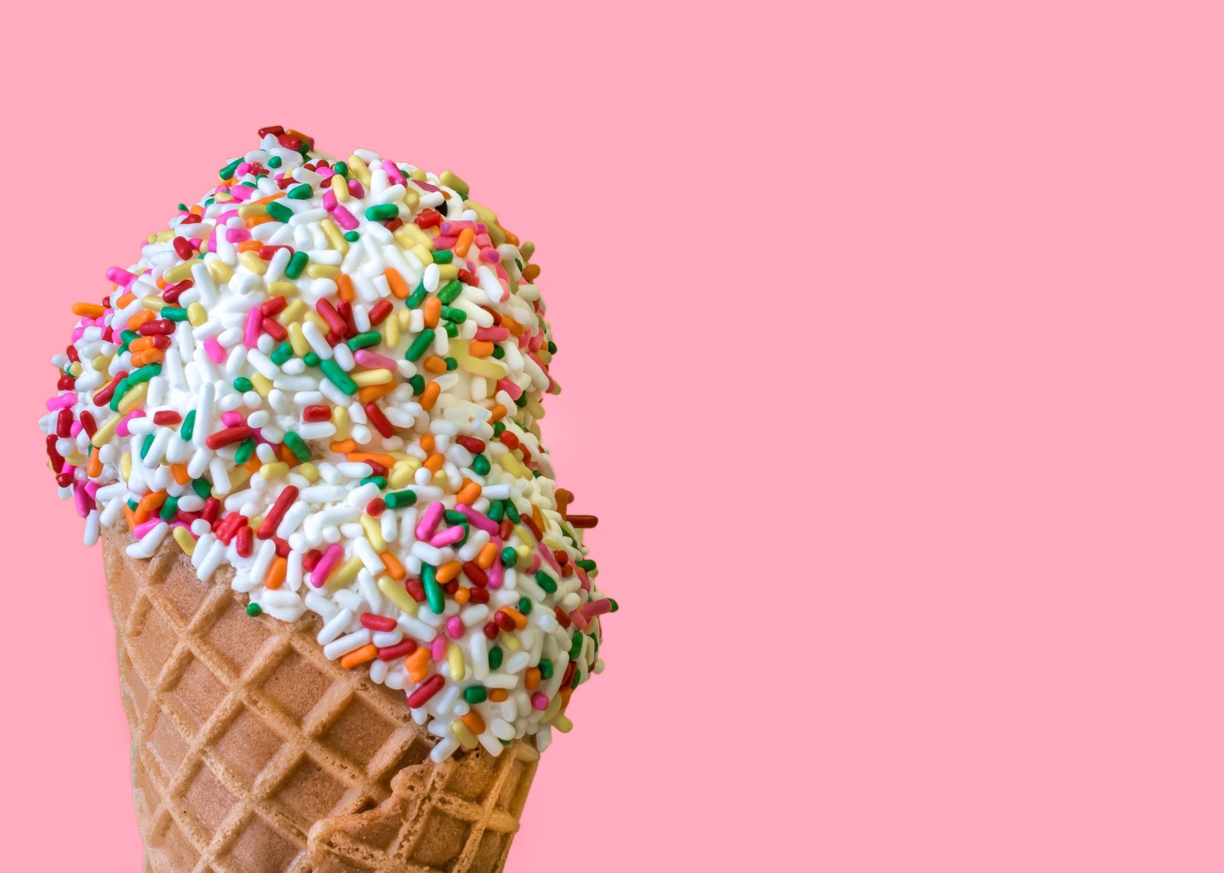 Ice cream scoop with sprinkles in a waffle cone on a light pink background.