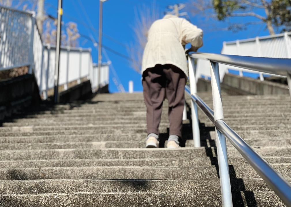 An elderly woman holding a handrail and going up the stairs.