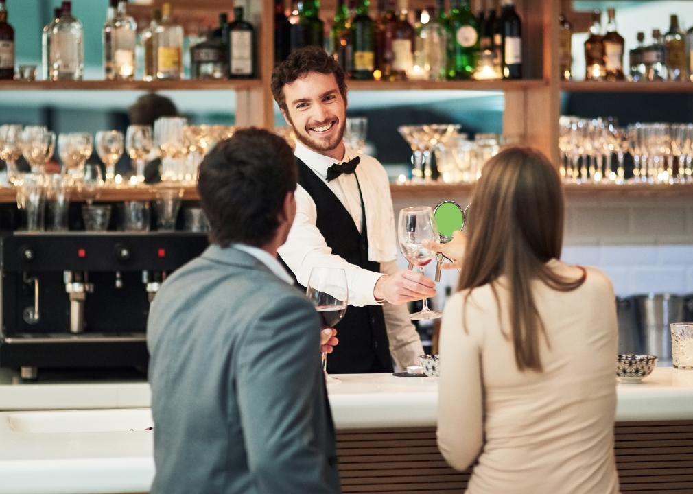 Bartender handing wine to customer sat at an upscale bar.