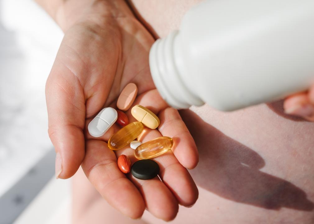 Closeup photo of someone pouring supplements from a white bottle into their palm.