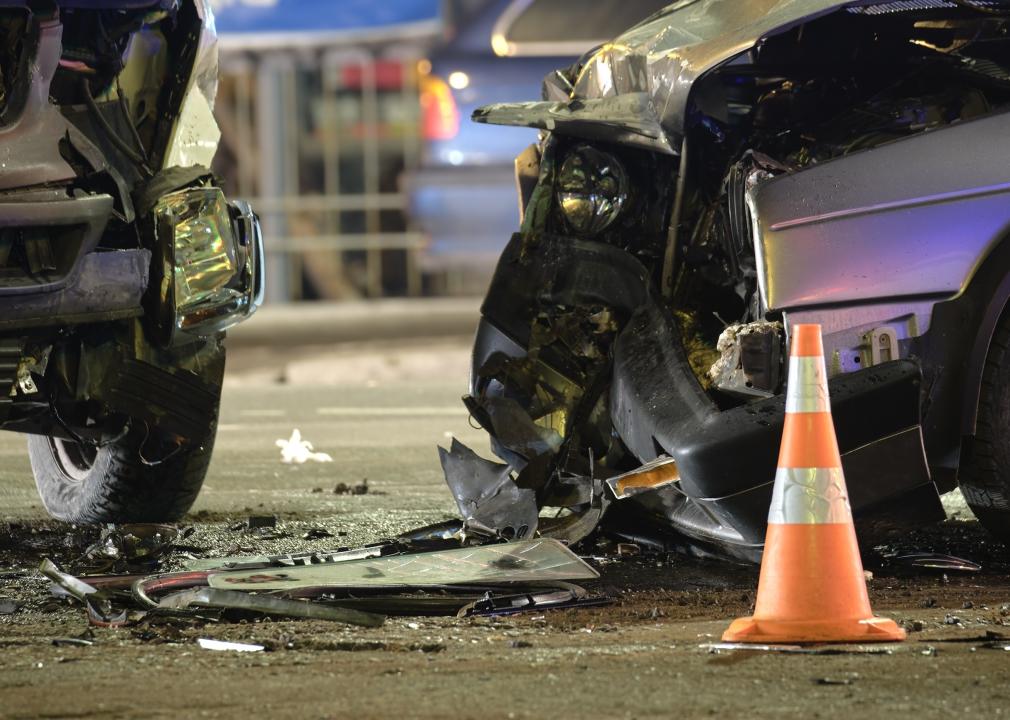 Two crashed cars and an orange traffic cone on a city street at night.