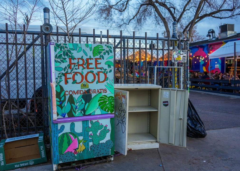 A fridge on sidewalk in an urban area that reads, free food, comida gratis.