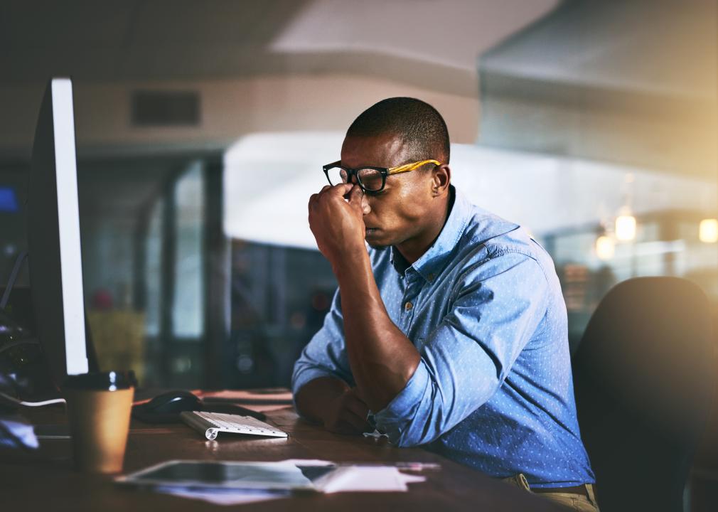 Stressed businessman pinching nose at night in office.