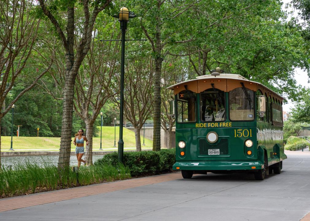 Woman jogging in a waterfront downtown area next to a trolley that has the words, ride for free, on it.