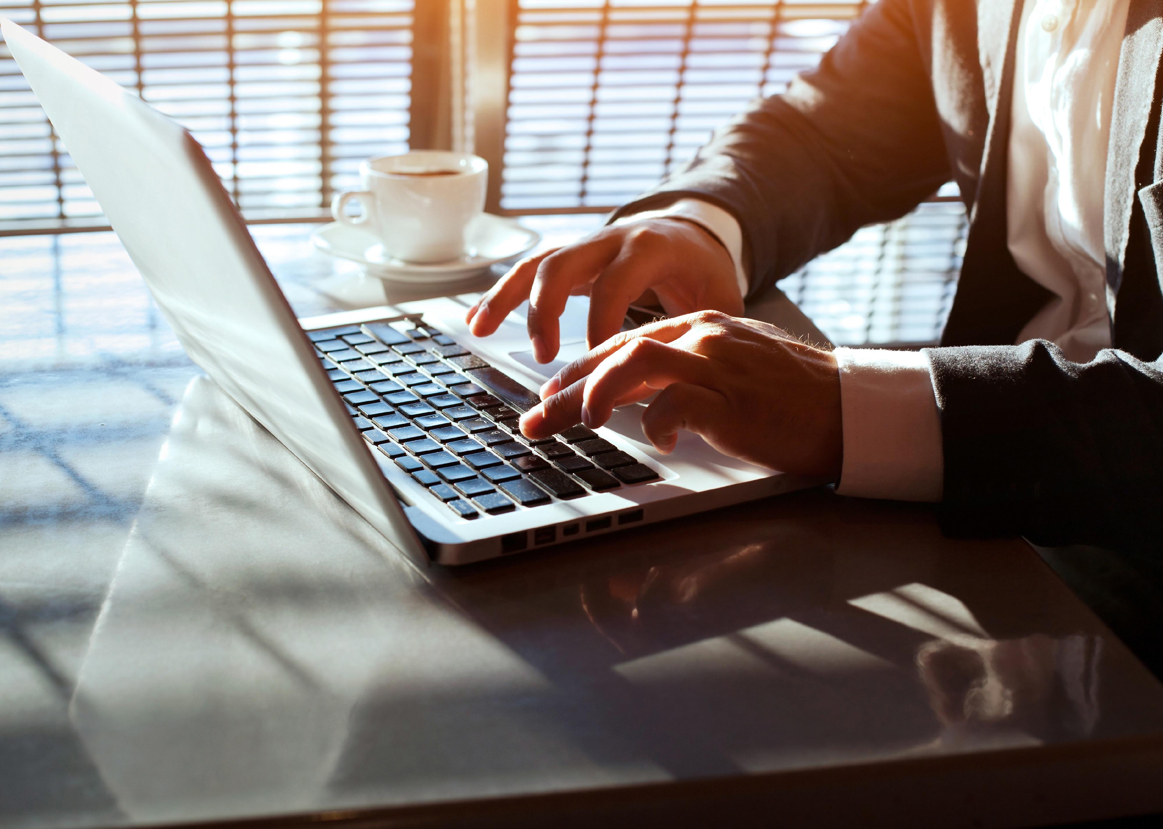 Close-up of a person's hands working on laptop.