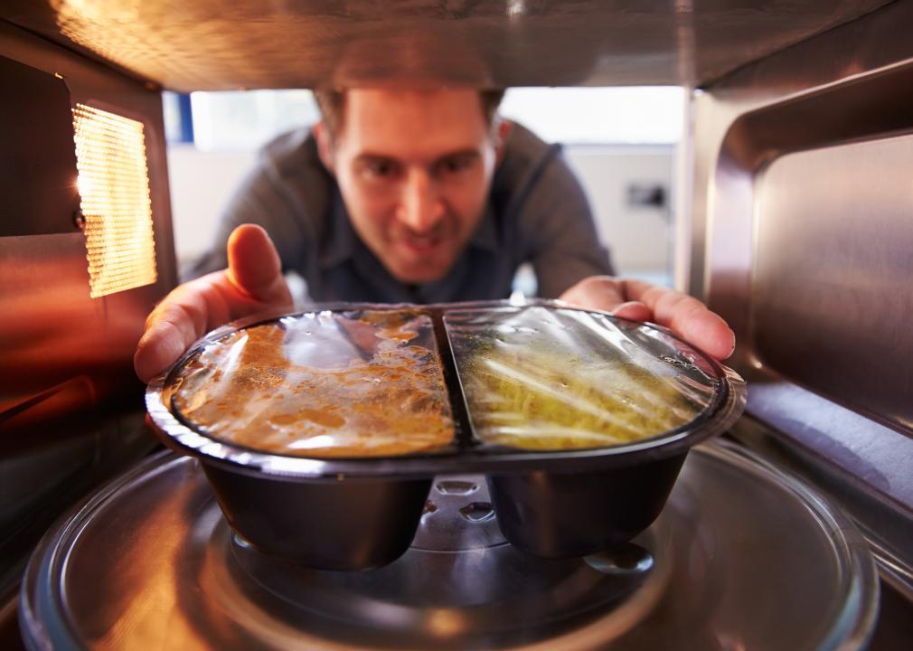 A man placing a TV dinner into a microwave.