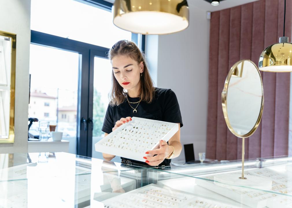 A woman placing jewelry in the glass case in a store.