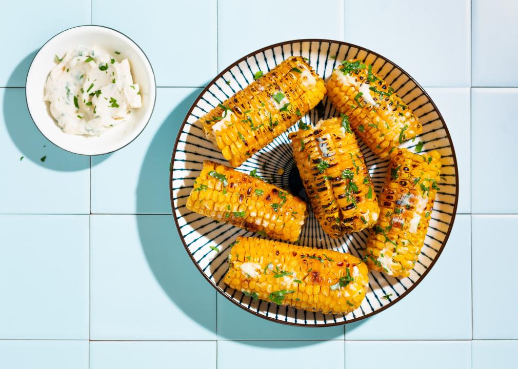 Grilled corn cobs with butter, cheese and herbs.