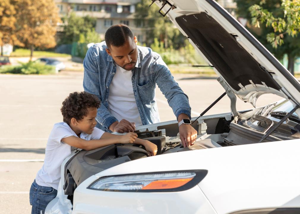 Father and son checking car engine outdoors.