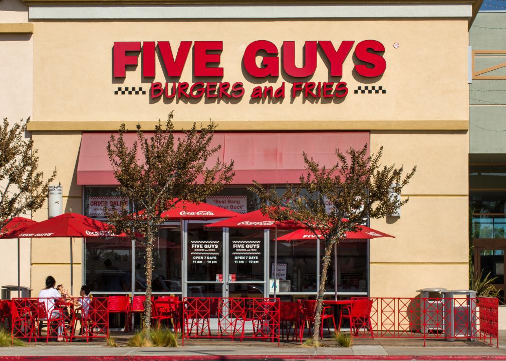 People sitting at a table with a red umbrella in front of a Five Guys.