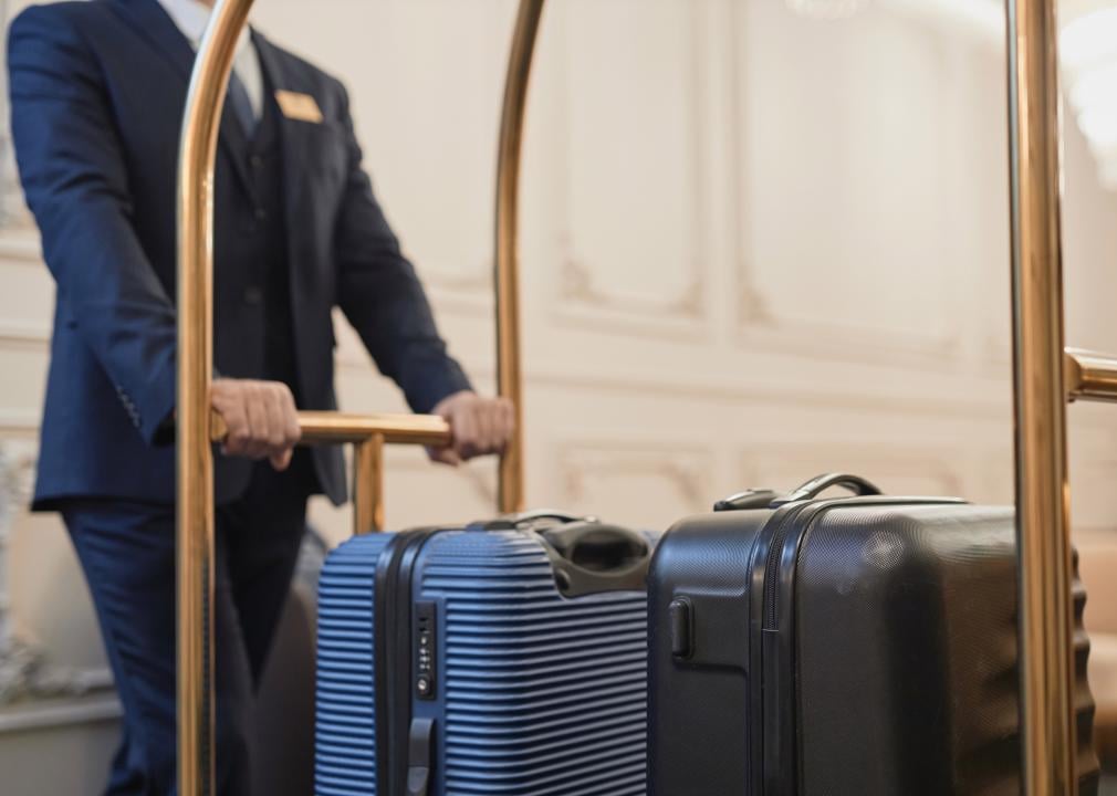 A porter wearing a suit pushing a cart with suitcases.