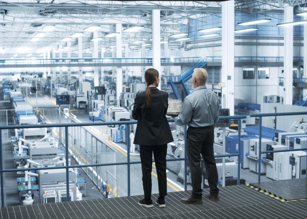 Two workers in business attire, overlooking a factory.