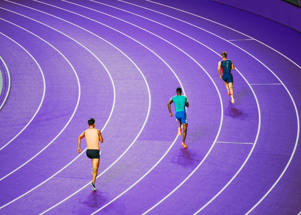 Three male sprinters on a purple track. 