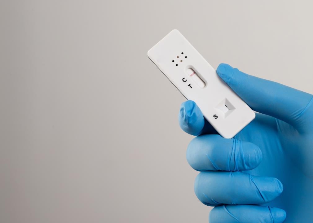 A hand with a blue glove holding a COVID-19 test with a red line next to the C. 