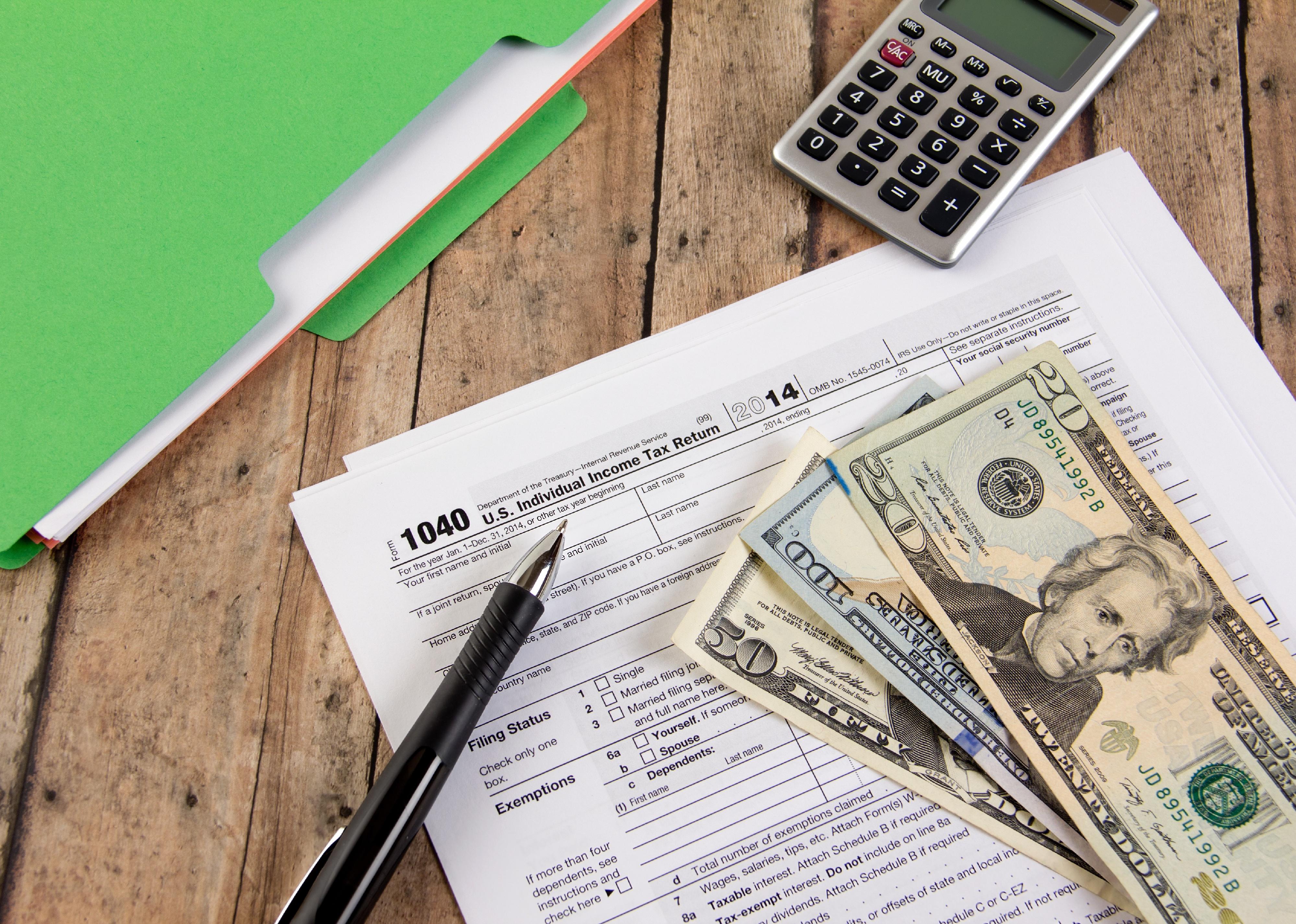 Tax form, cash and calculator on a wooden bench.