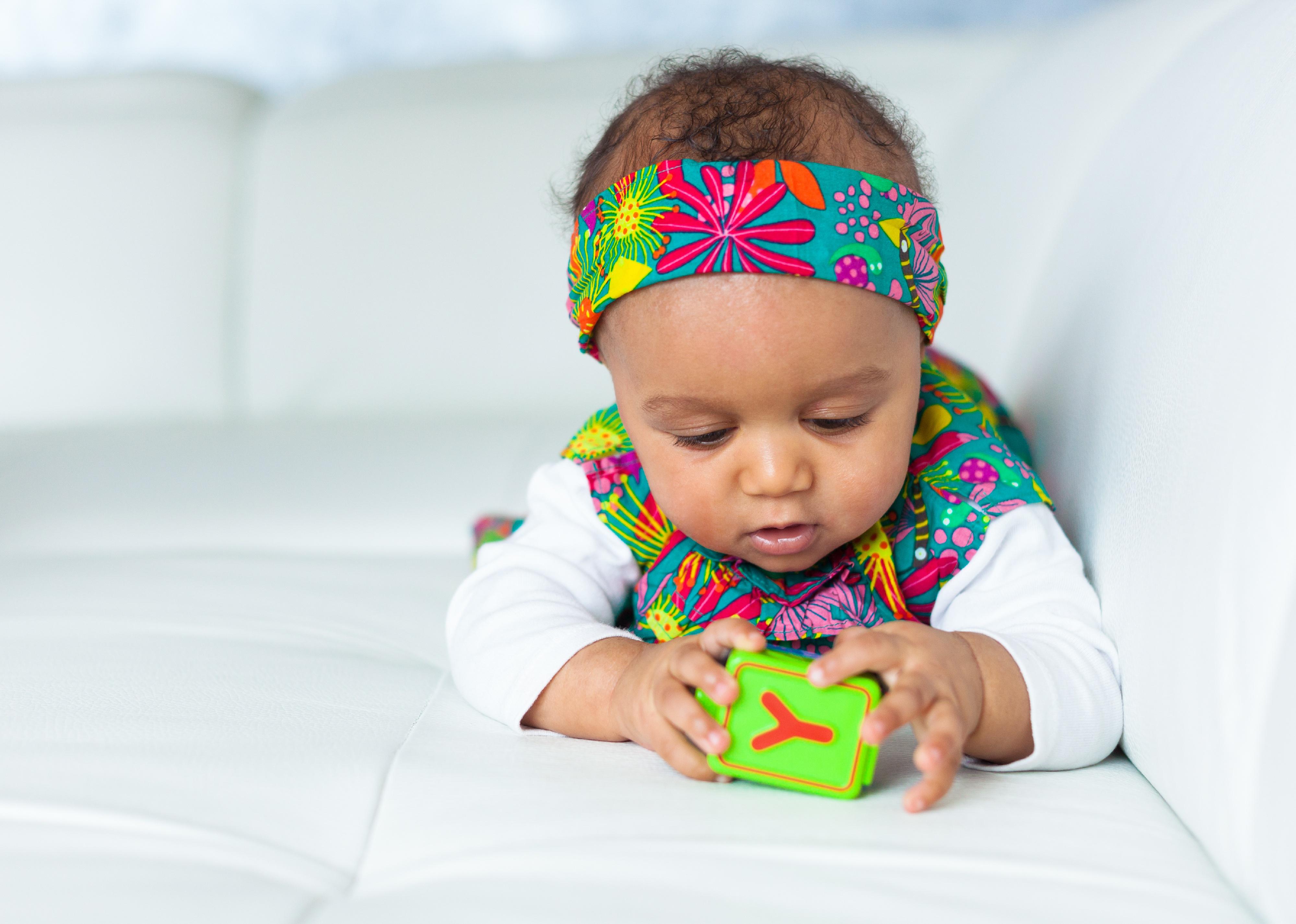 Baby wearing colorful headband playing with toy.