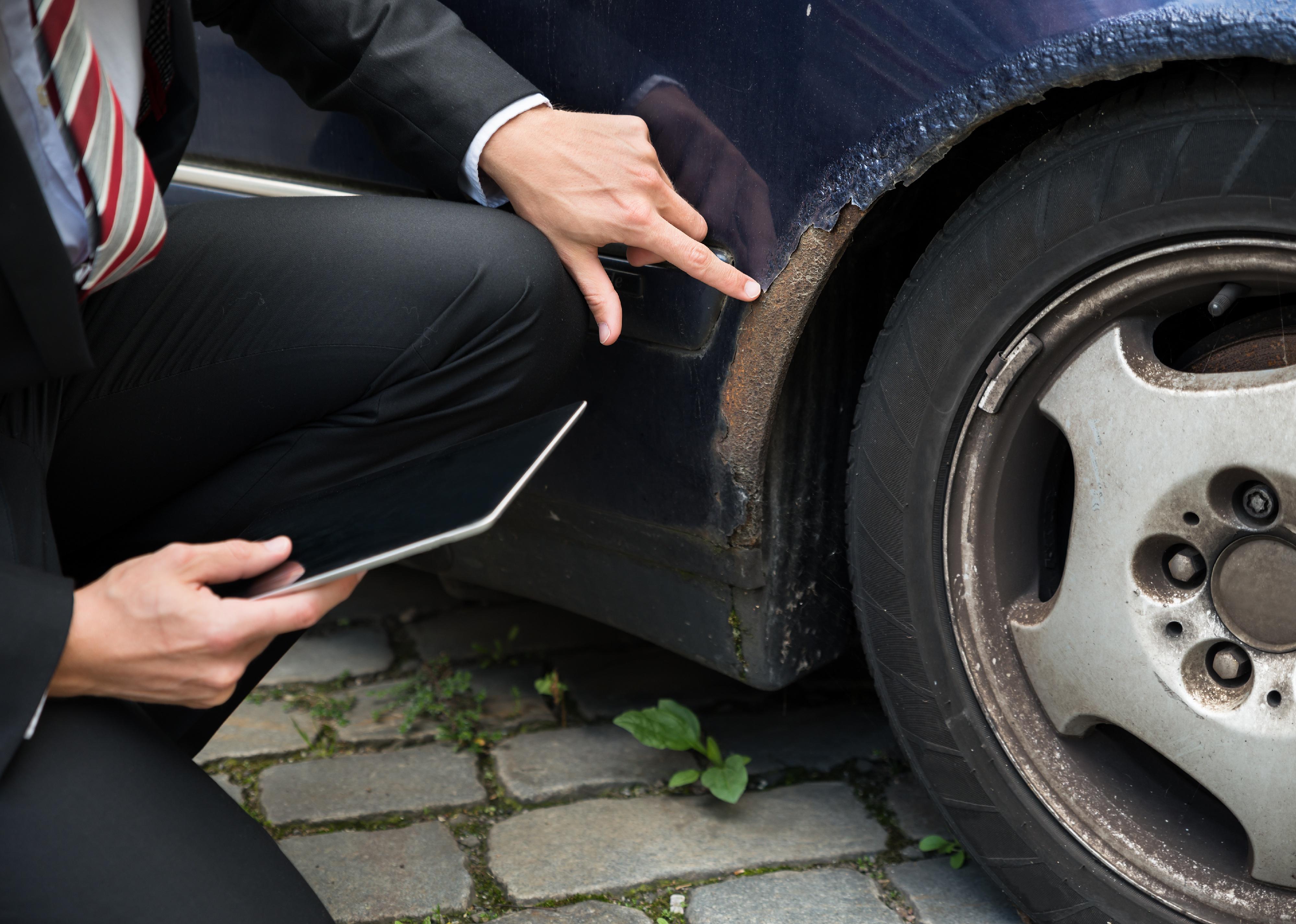 Insurance agent holding tablet examining car damage