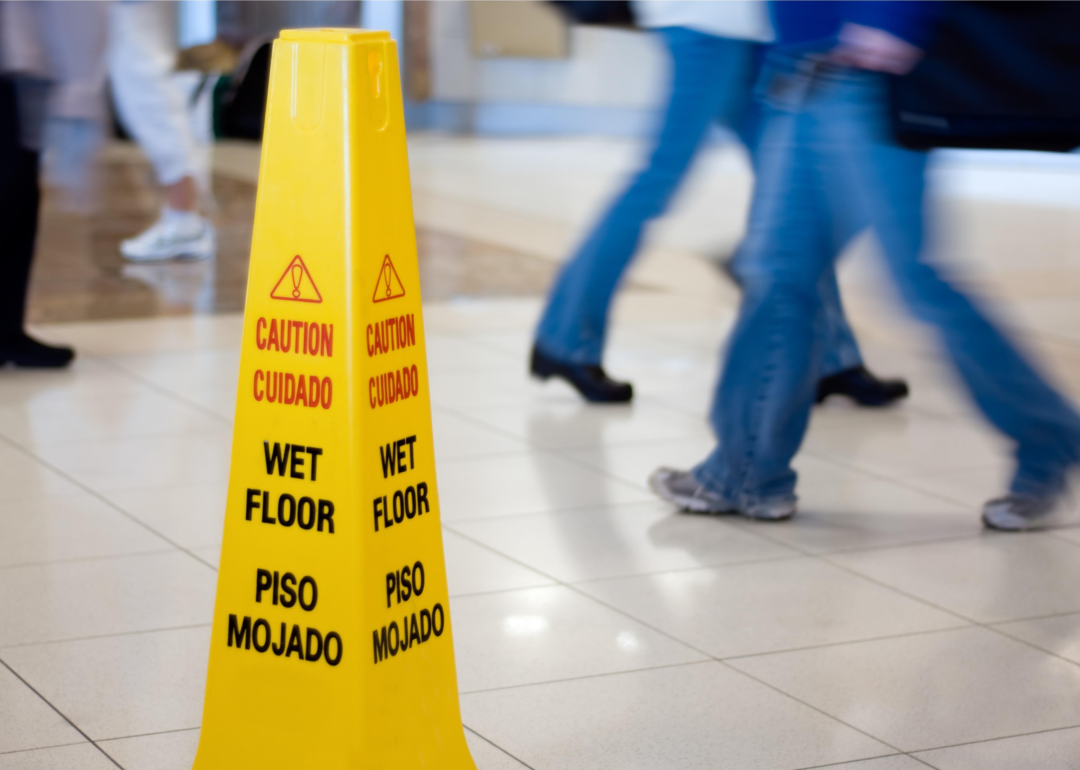Caution Wet Floor sign with people walking in the background.