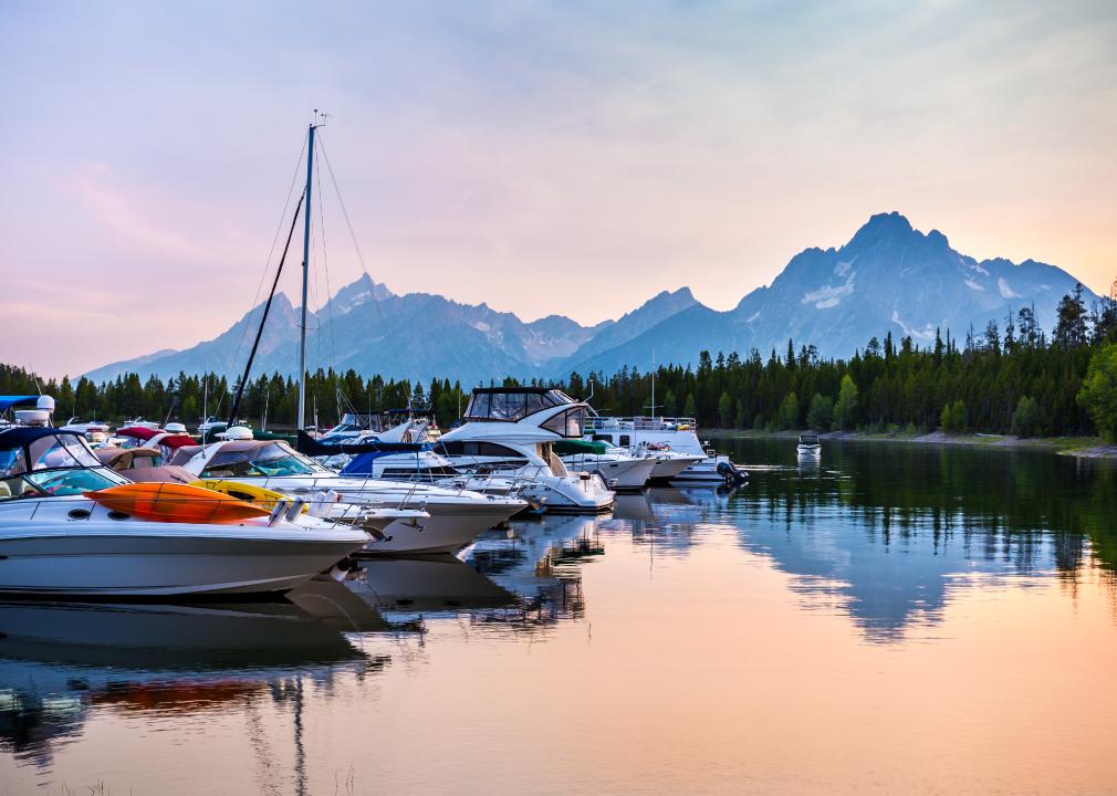 Boats on a lake at sunset in Colter Bay with Grand Teton Mountains.