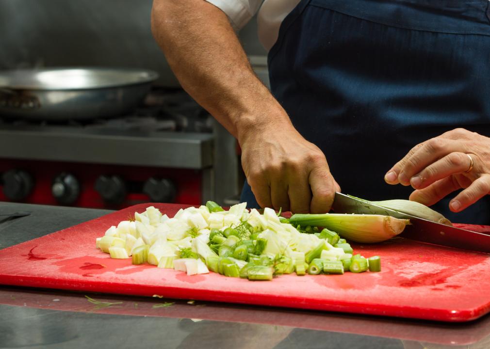 A worker chipping celery on a chopping board in a commercial kitchen.