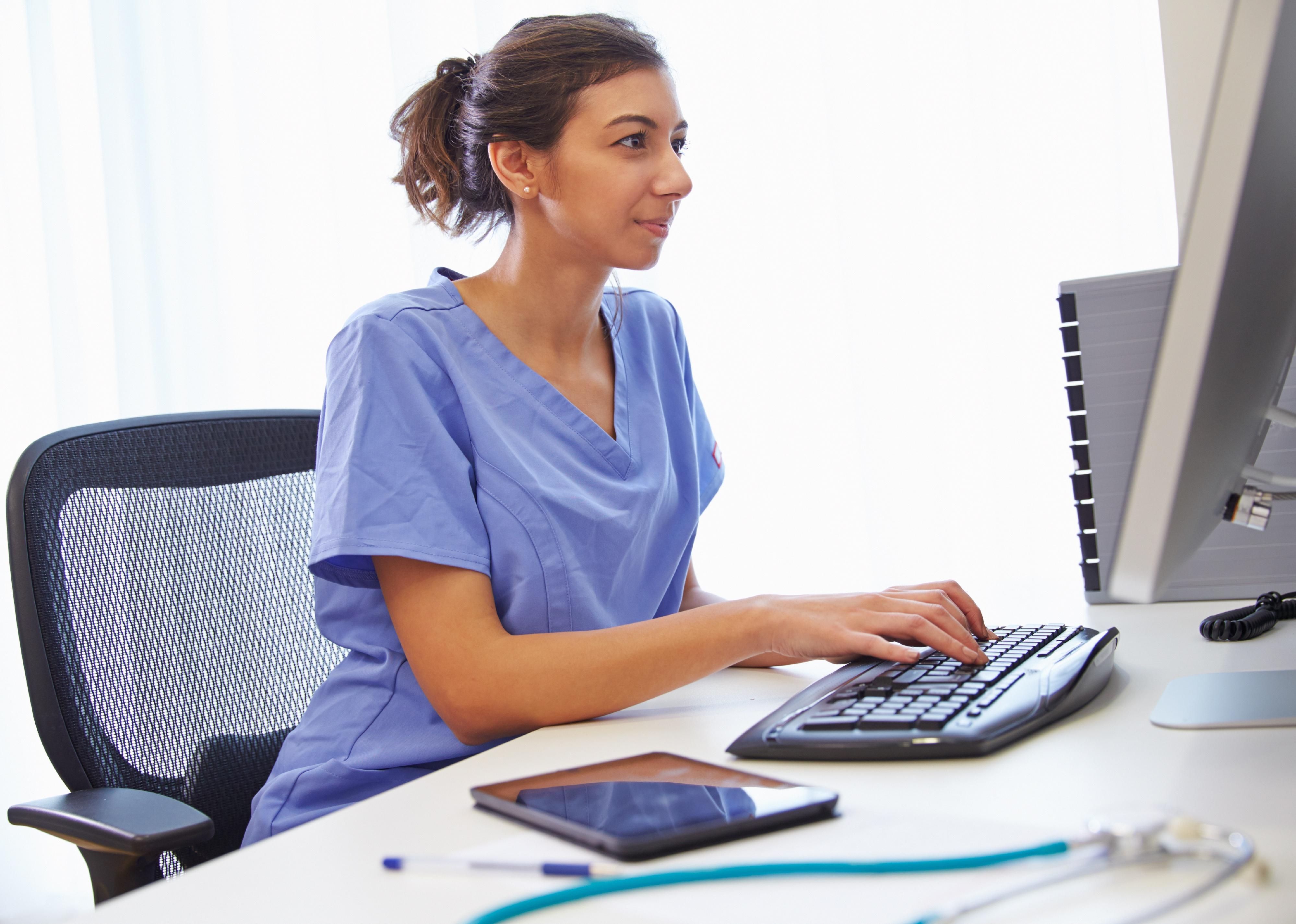 A women in scrubs at a computer.