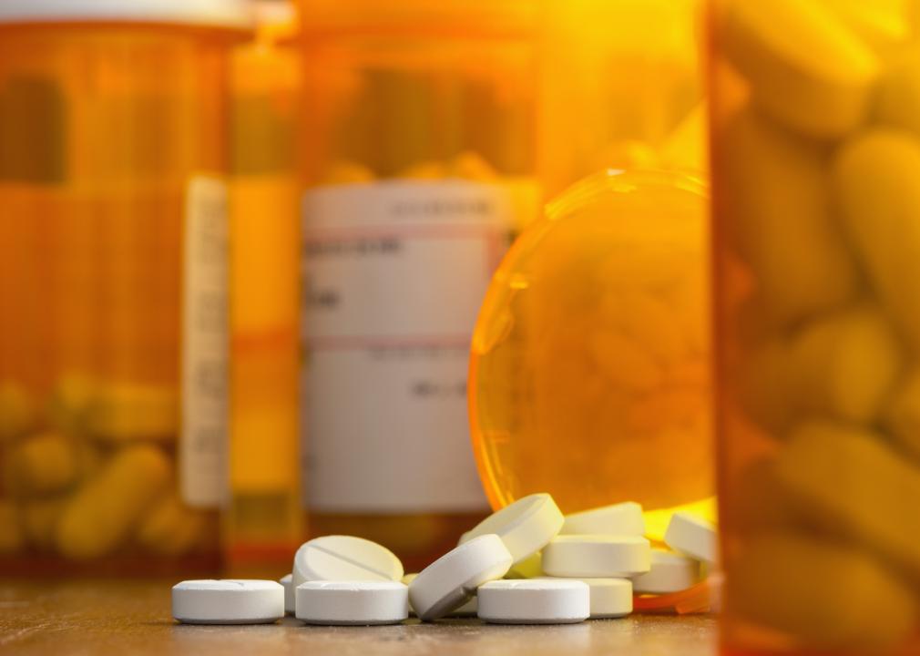 Prescription painkillers spilling from a bottle on a table with other bottles out of focus.