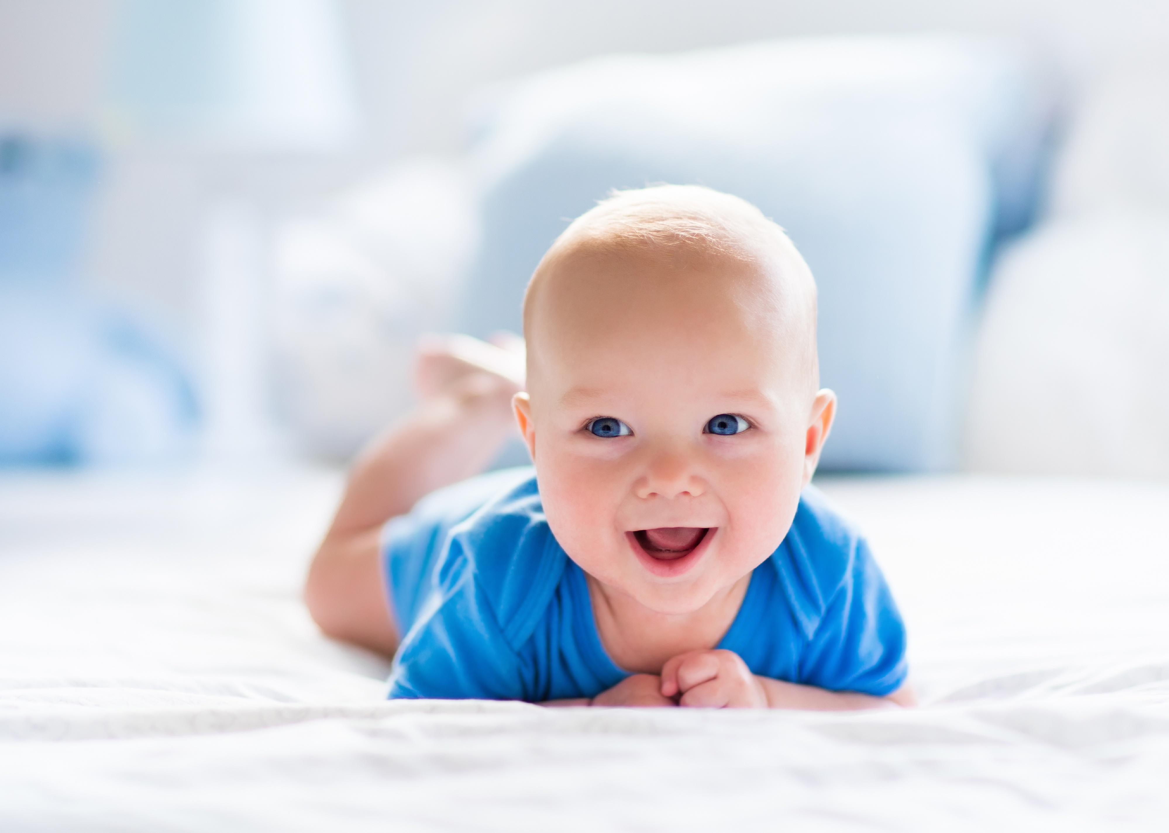 Cute baby in blue clothing laying on stomach.