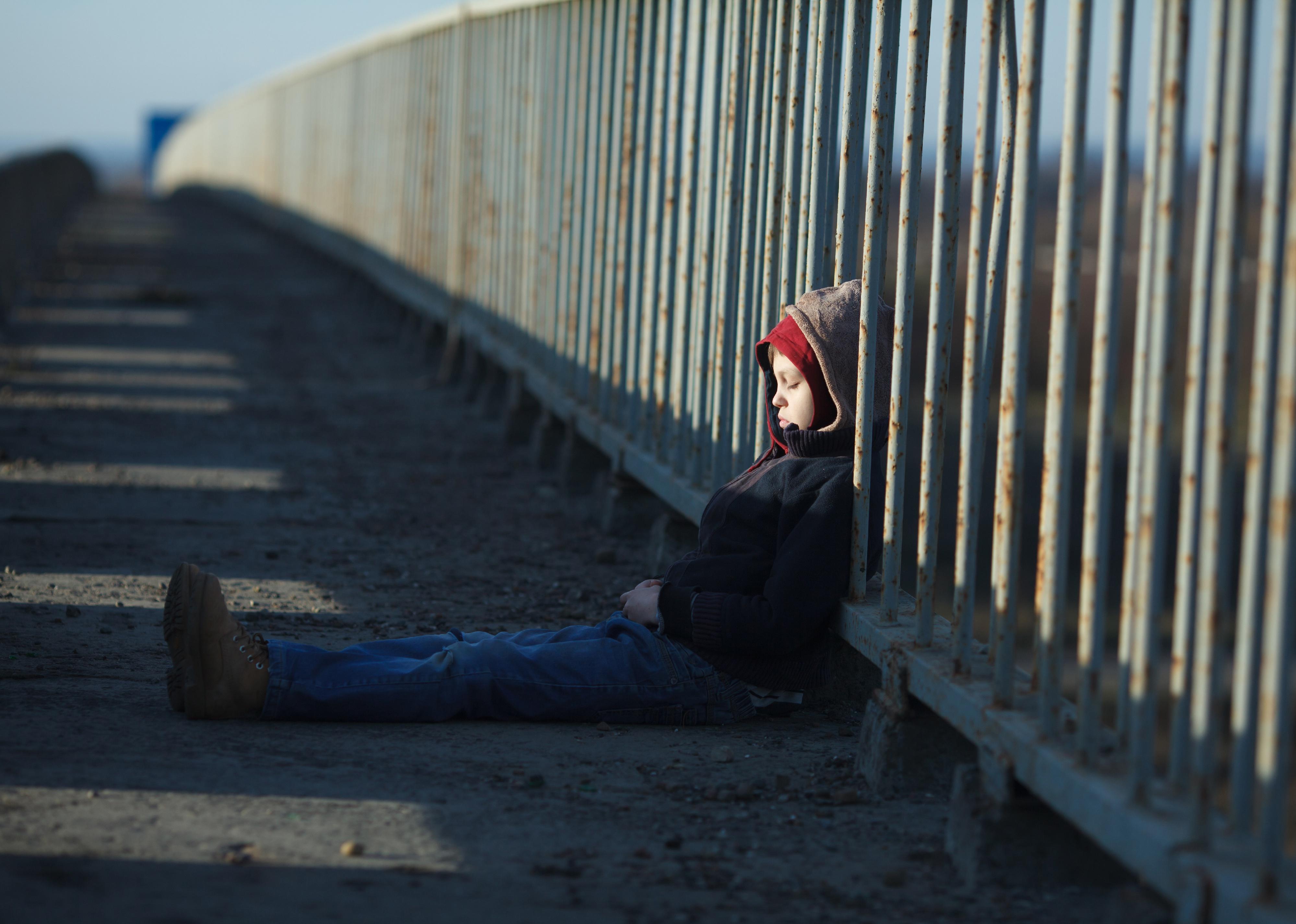 Young homeless boy sleeping on a bridge.