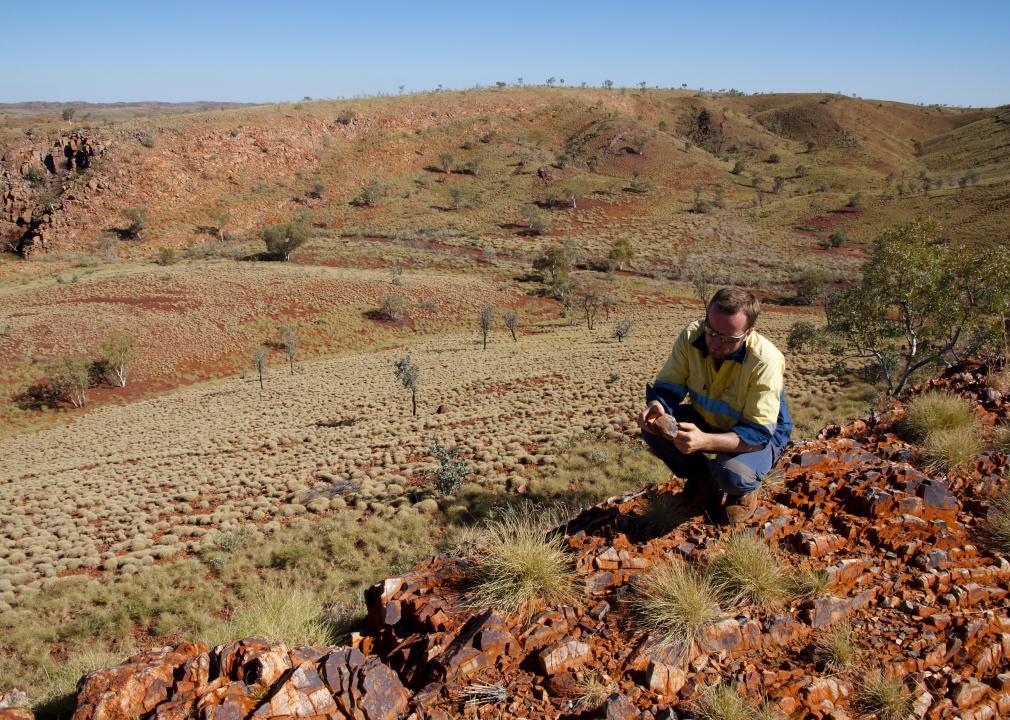 A man looks at a rock in a desolate landscape.