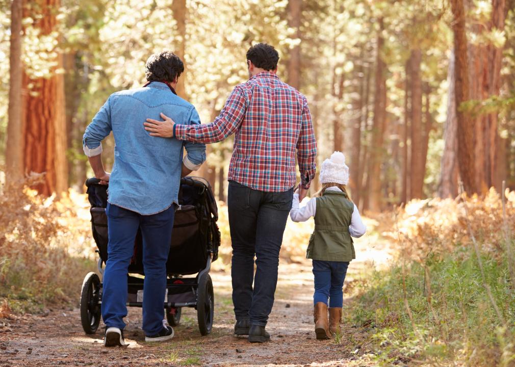 Two men walking in woods, one pushing buggy, the other holding a little girl's hand