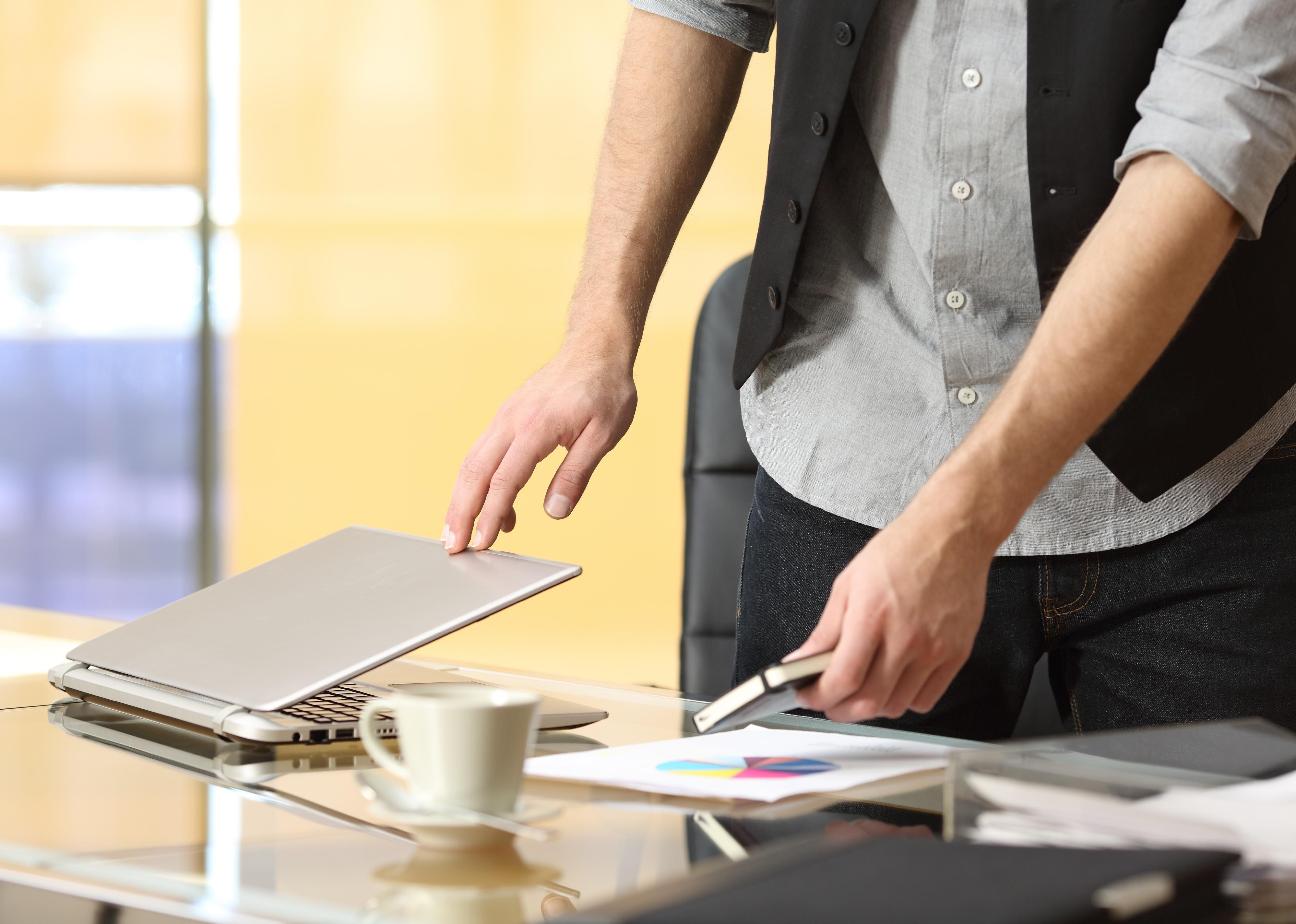 Close-up of a businessperson's hands leaving work and closing laptop at office.