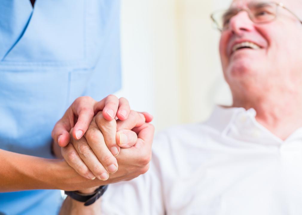 Nurse holding hand of senior man in home.
