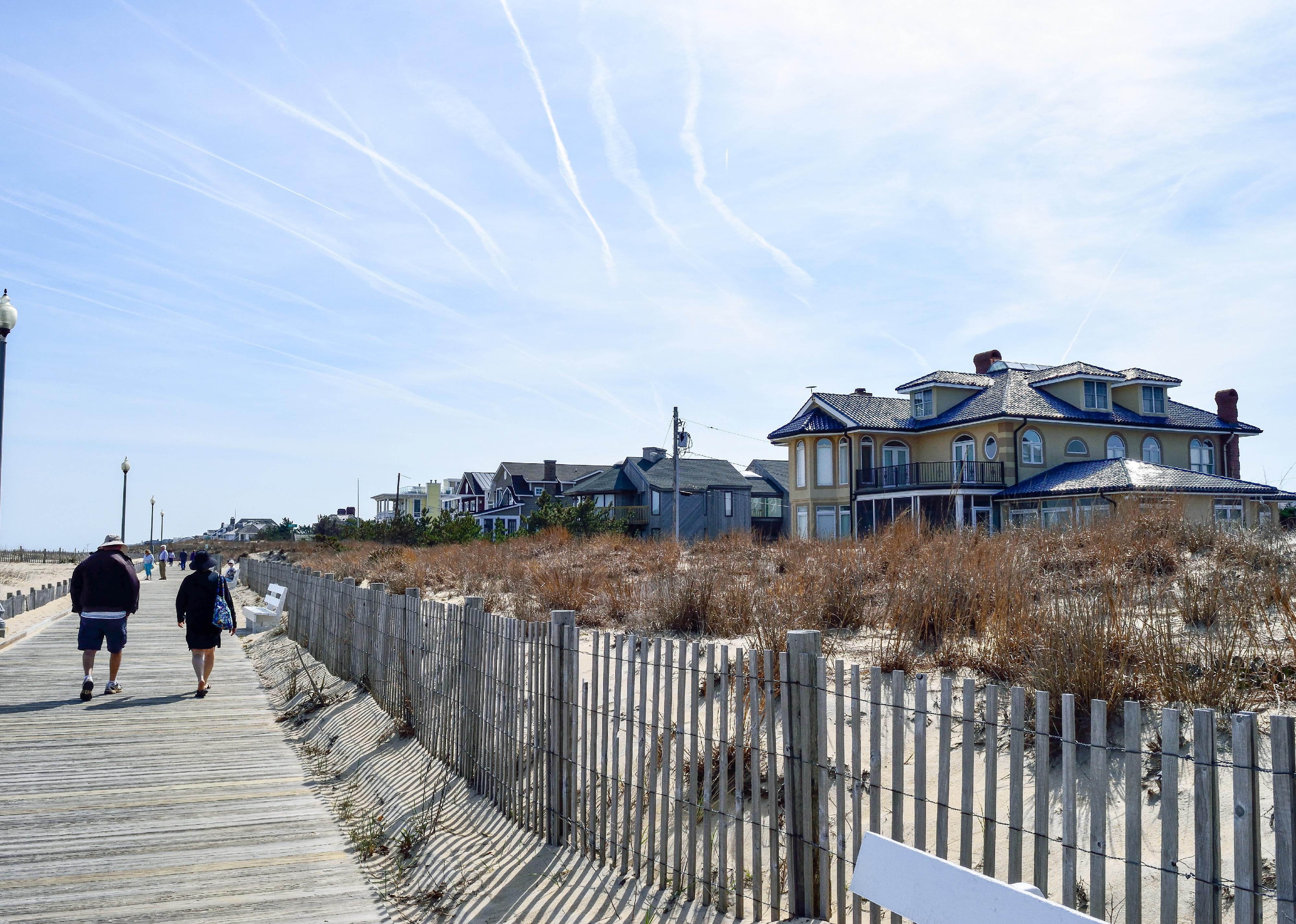 People walking on boardwalk by dunes and homes.