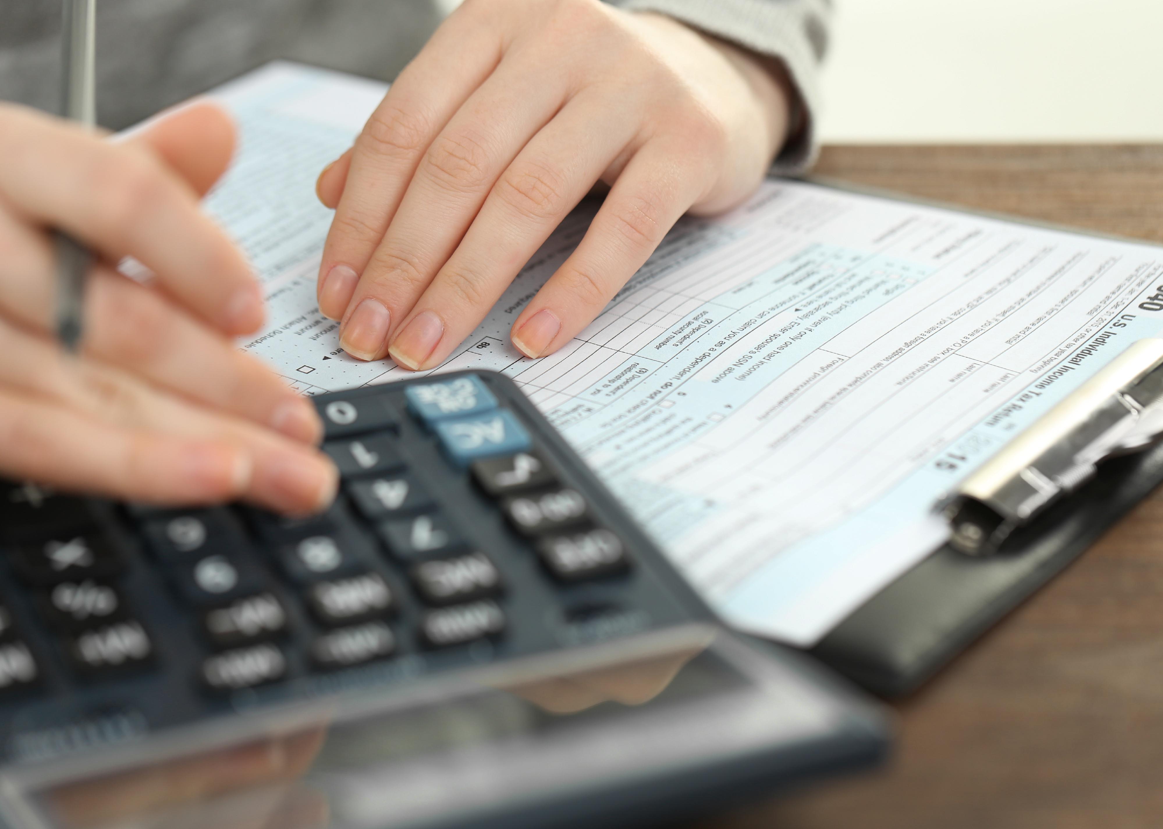 Female hand holding a pen and using calculator while filling in a income tax return.